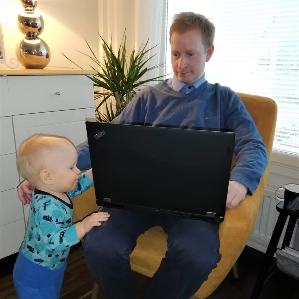Olli Lehtonen istuu nojatuolissa läppäri sylissä ja Filip-vauva pyrkii syliin.