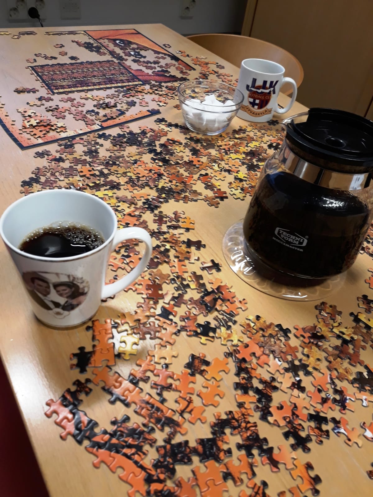 Pöydällä tekeillä oleva palapeli, mukit ja kahvipannu.