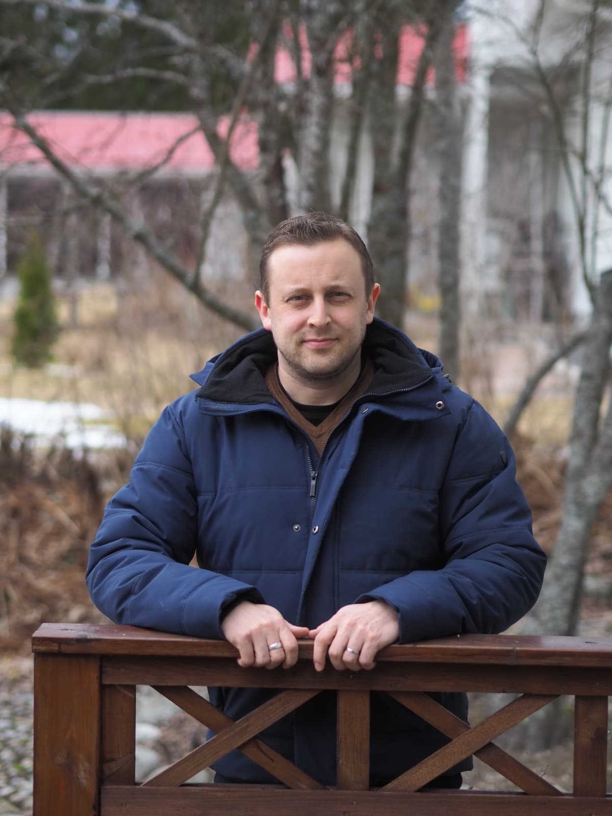 Valtio-opin dosentti Jouni Tilli nojaa puisen aidan kaiteeseen molemmilla käsillään, päällään tummansininen toppatakki. Taustalla syksyistä vesakkoa.