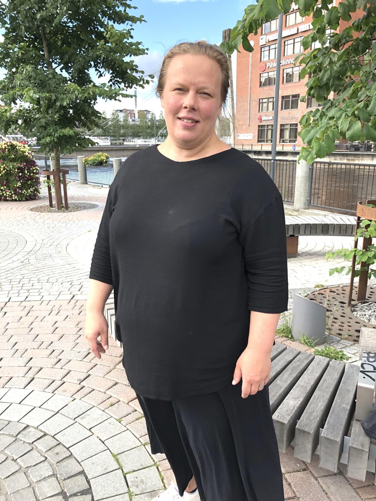 Nainen seisoo punatiilirakennuksen edessä, aukiolla.