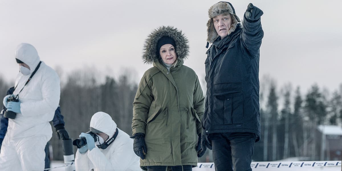 Sorjonen (Ville Virtanen) osoittaa sormella kuvan ulkopuolelle. Lena Jaakkola (Anu Sinisalo) katsoo sormen osoittamaan suuntaan, taustalla rikospaikkatutkijoita valkoisissa puvuissaan.