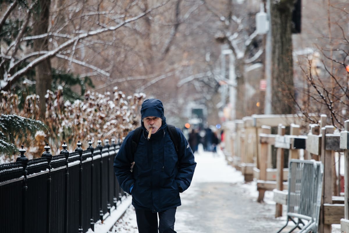 Talvivaatteisiin pukeutunut mies sikari suussa kävelee lumisella kadulla New Yorkissa.