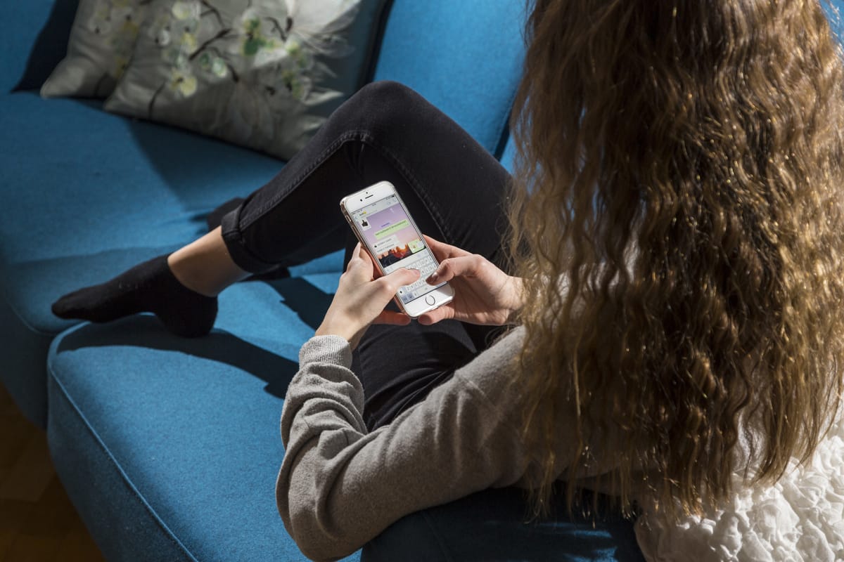 Nuori istuu sohvalla ja naputtelee Whatsappia.