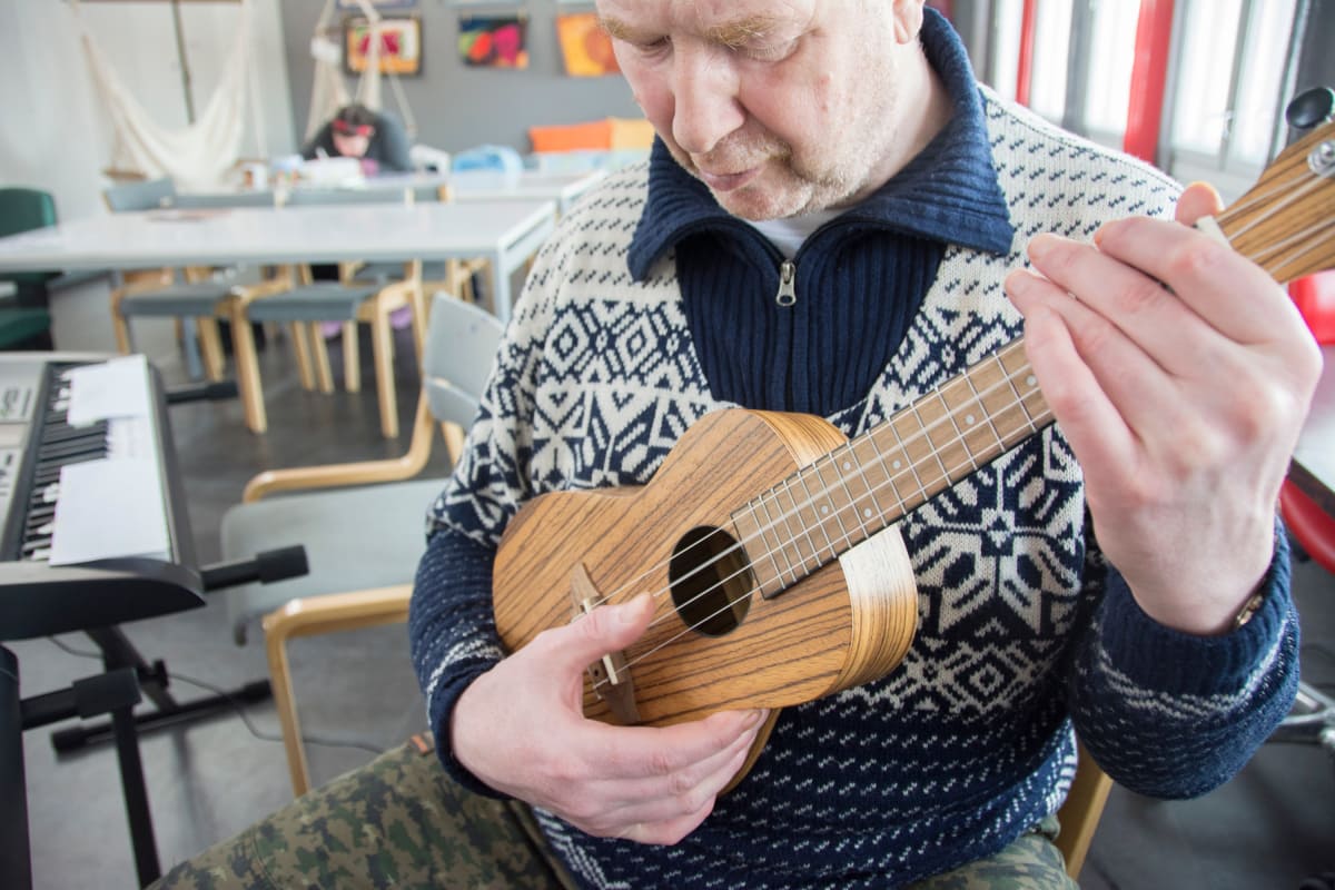 Heimo Suvanto soittaa ukulelea keskittyneenä.