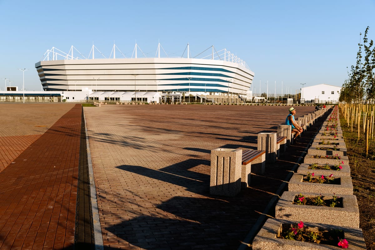 Kaliningradin uusi stadion ilta-auringossa. Etualalla on penkkirivistö, jossa istuu mies.
