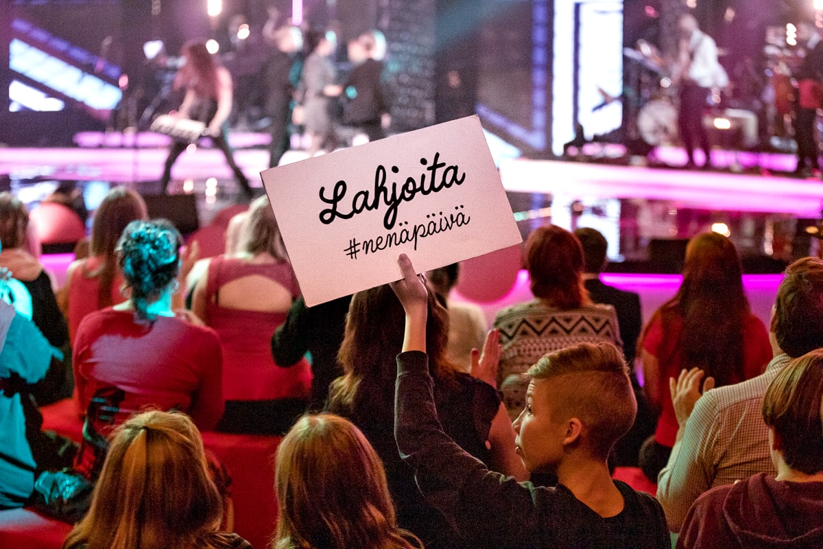 Nenäpäivän televisiolähetyksen yleisöä. Naisella on kädessään kyltti jossa lukee "Lahjoita #nenäpäivä".