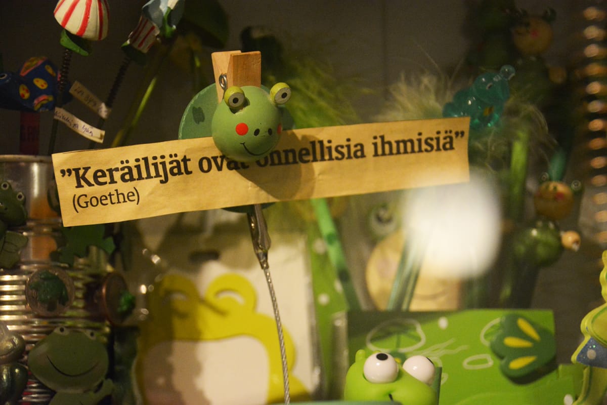 Koristesammakon suussa paperilappu, jossa lukee mietilause: Keräilijät ovat onnellisia ihmisiä