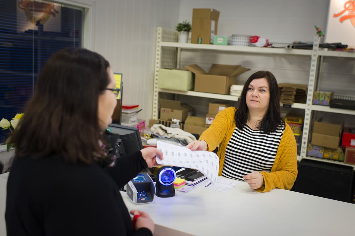 Tiina Mäkihonka palvelutiskin takana ojentaa papereita asiakkaalle.