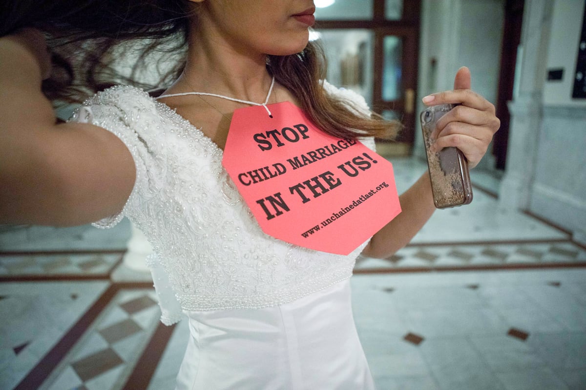 Kuvassa on nuori nainen, jonka kaulassa on kyltti, jossa lukee: Stop child marriage in the us!