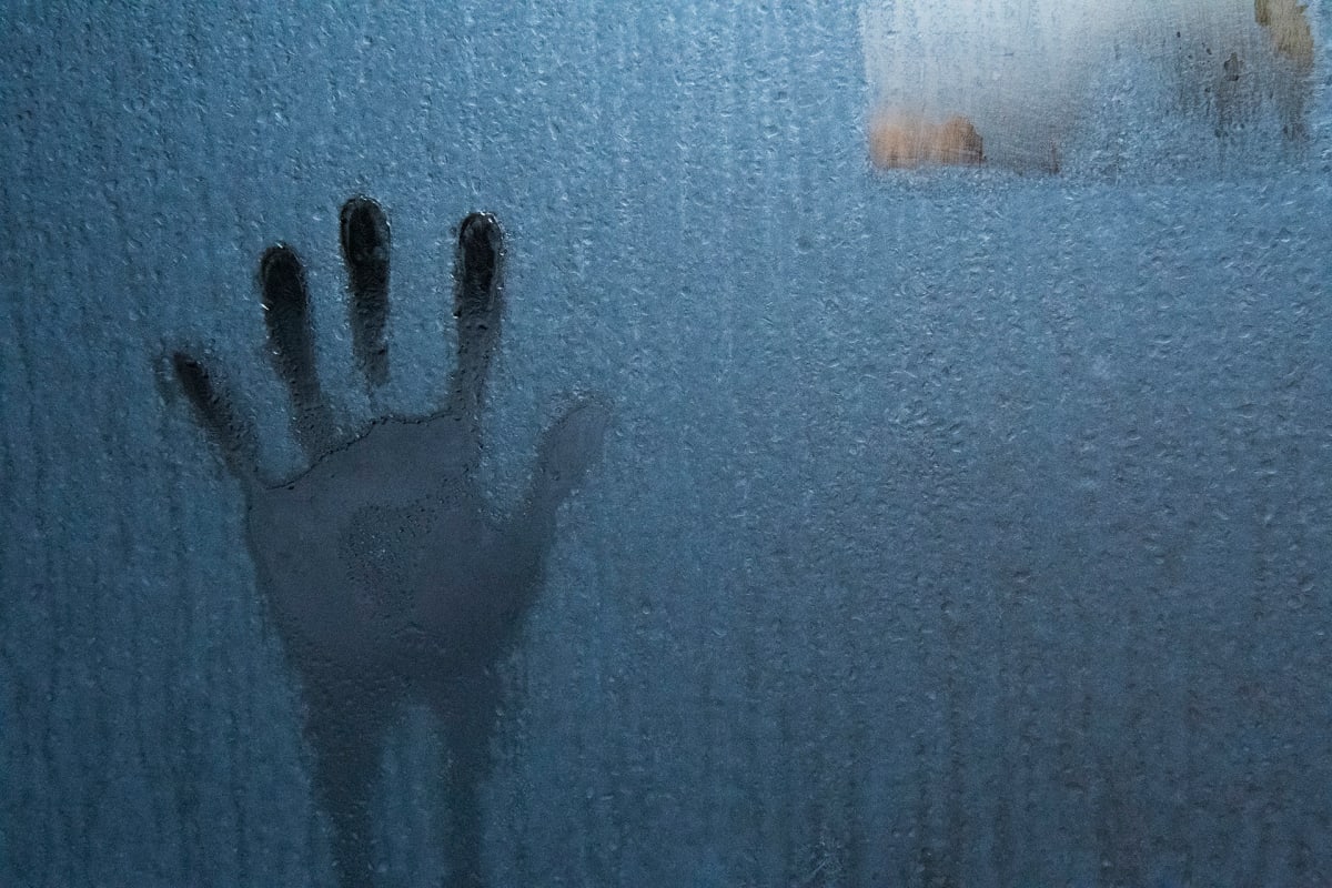 Käden kosketuksen jälki huurteisessa lasiseinässä.