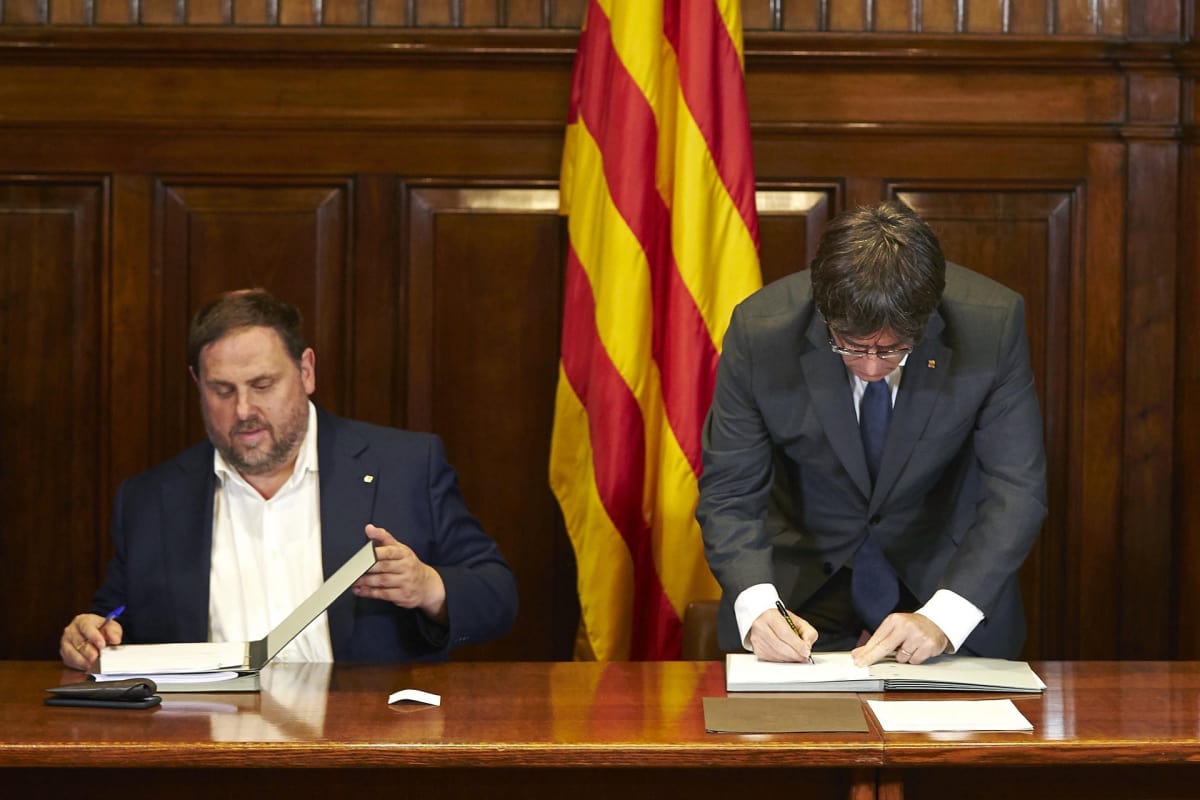 Katalonian aluehallinnon johtaja Carles Puigdemont (oik.) allekirjoittamassa asetusta itsenäisyyskansanäänestyksestä. Vieressä istuu aluehallinnon varajohtaja Oriol Junqueras.