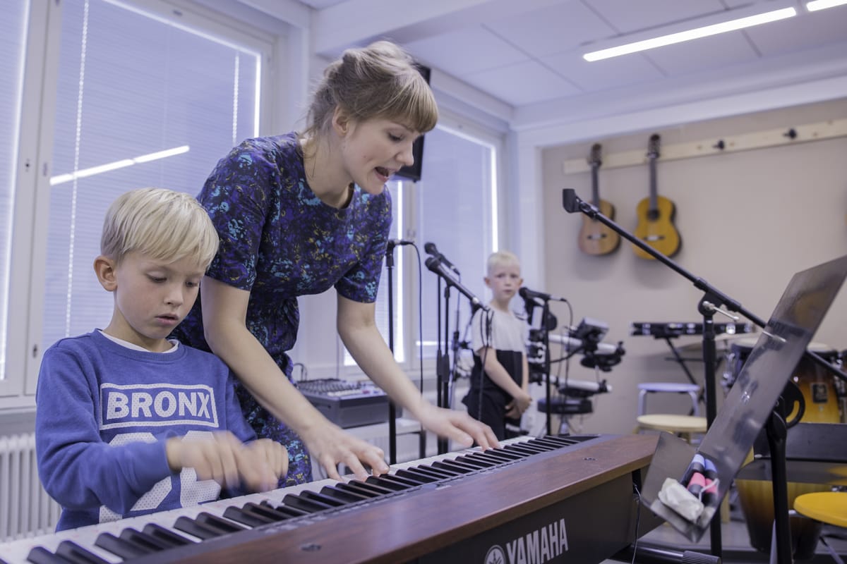 Musiikinopettaja Ella Rosenlund neuvoo Ekko Pakkasta koskettimissa. Taustalla laulaa Niilo Käenmäki.