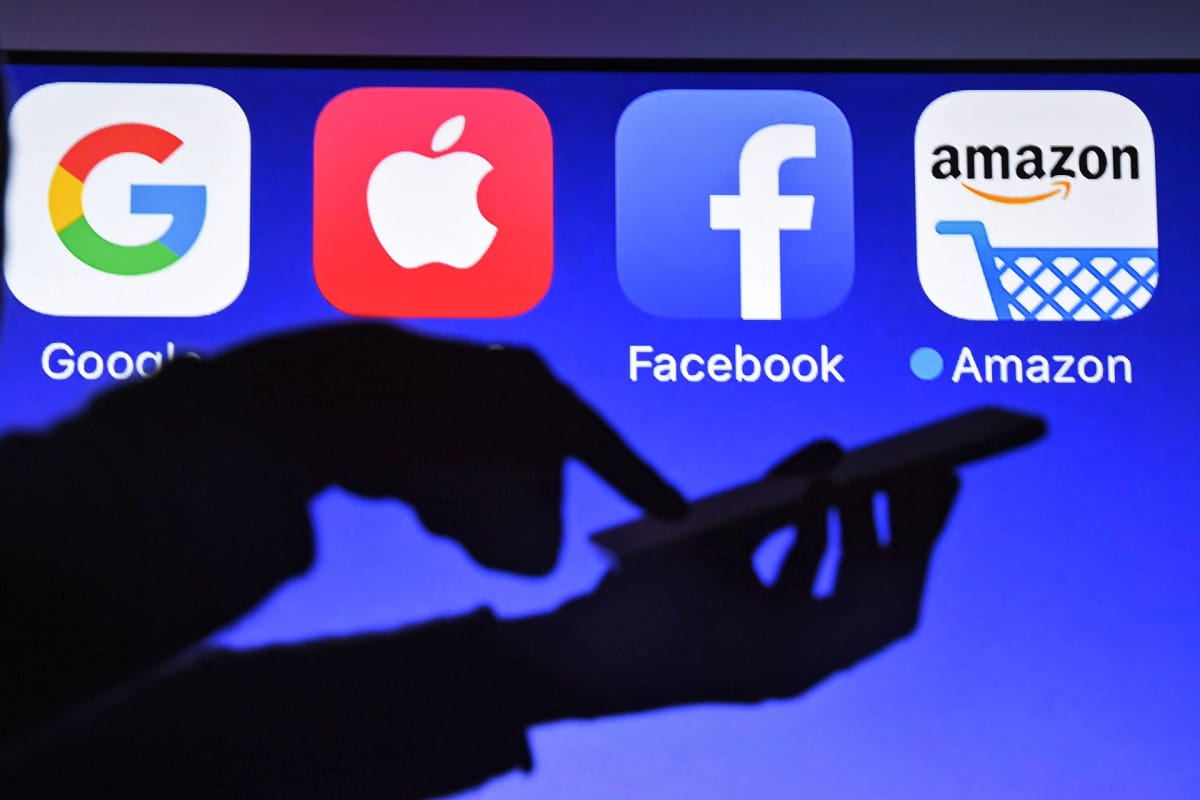 Miehen kädet siluetissa sinistä taustaa vasten. Takana näkyvät Googlen, Applen, Facebookin ja Amazonin logot.