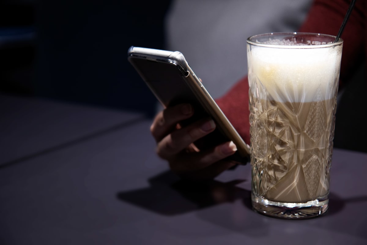Latte-kahvi, naisen käsi ja älypuhelin.