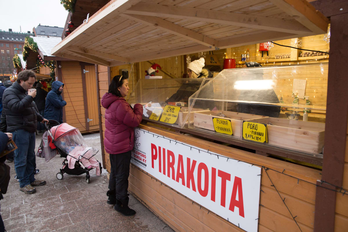 Turistit katselevat karjalanpiirakoita kojun edessä.