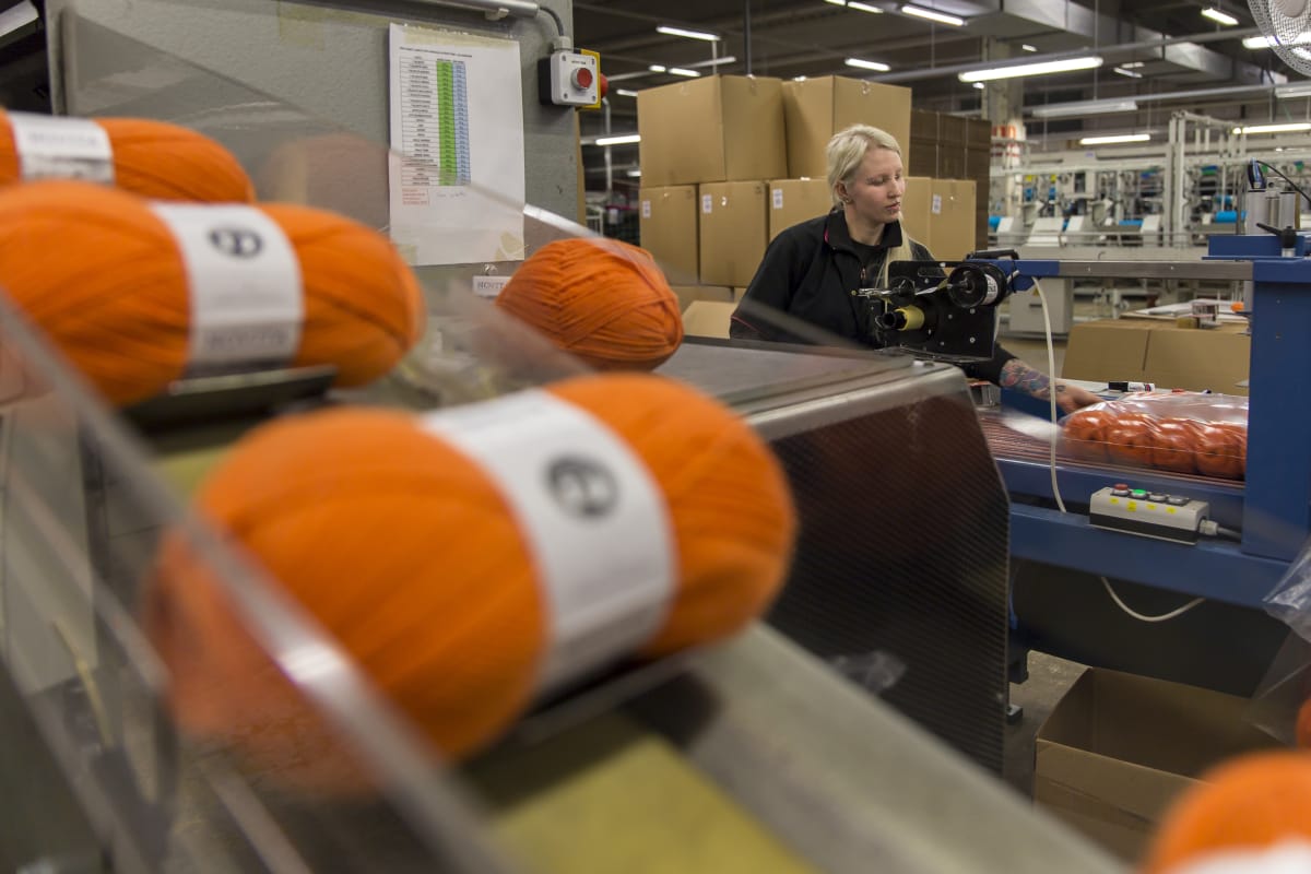Eveliina Laukkanen pakkaa oransseja villalankakeriä Novitan tehtaalla.
