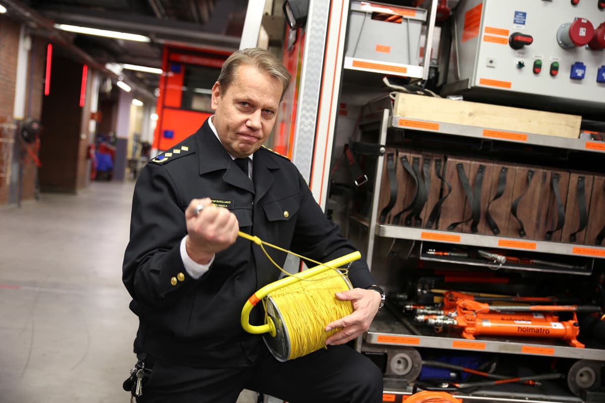kuvateksti: Helsingin kaupungin pelastuslaitoksen viestintäpäällikkö Taisto Hakalalla on kädessään kela, jossa olevaa narua palomies vetää mukanaan savusukeltaessaan maanalaiseen tilaan.