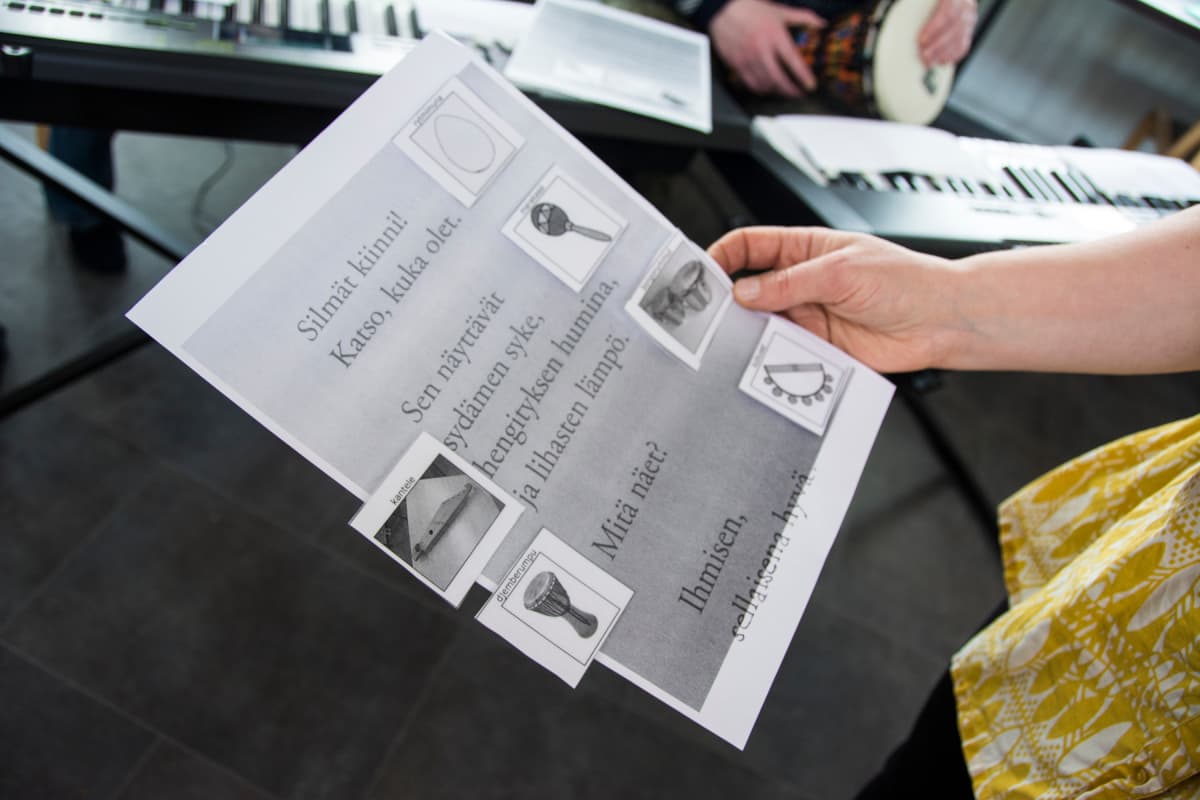 Yhteisömusiikin opettaja pitelee käsissään runoa, johon on kiinnitetty kuvia erilaisista soittimista.