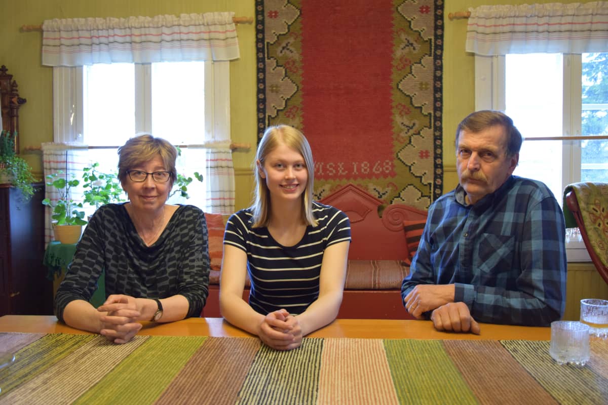 Vanhemmat istuvat tuvan penkillä tytär välissään.