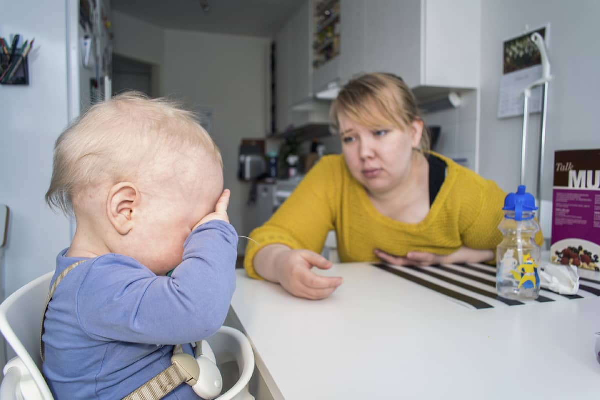 Lapsi istuu syöttötuolissa ja pitää kättä silmillään