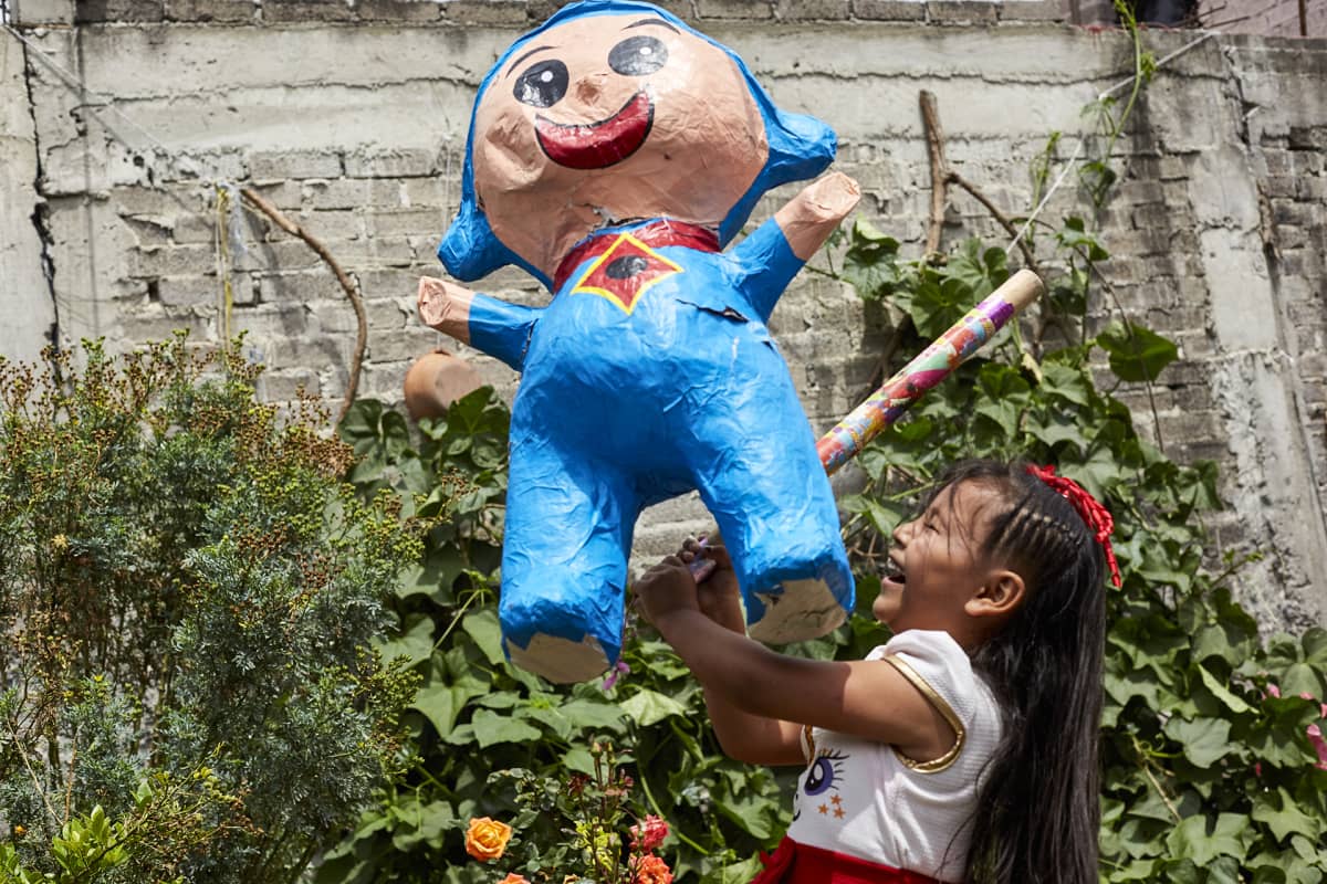 Tyttö lyö karkilla täytettyä piñata-nukkea lastenjuhlissa Chalcossa.