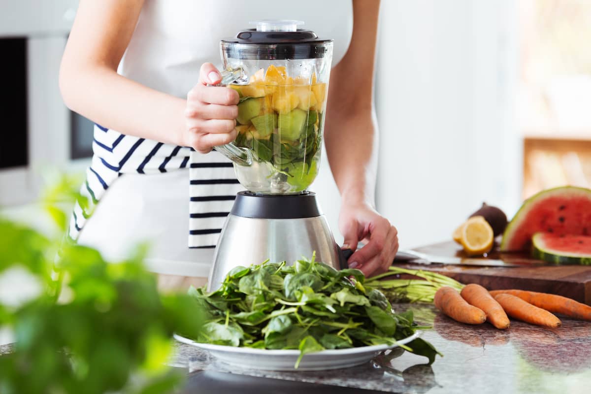 Nainen tekemässä smoothieta kasviksista ja hedelmistä.