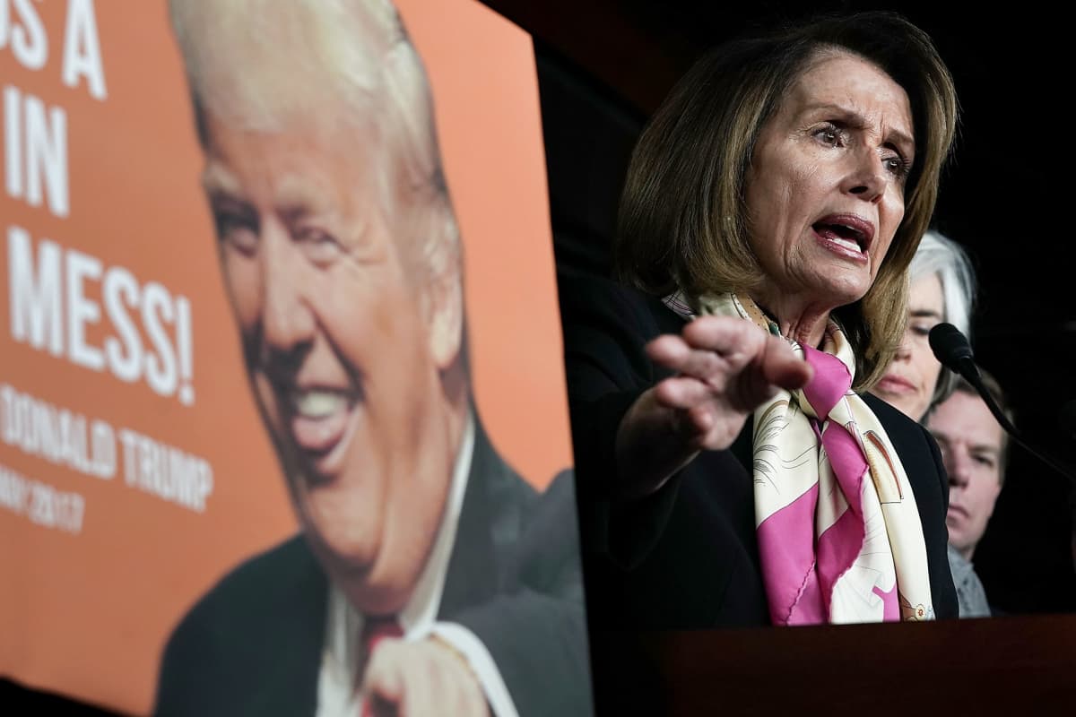 Lähikuva Nancy Pelosista ja julisteesta, jossa on Donald Trumpin kuva.