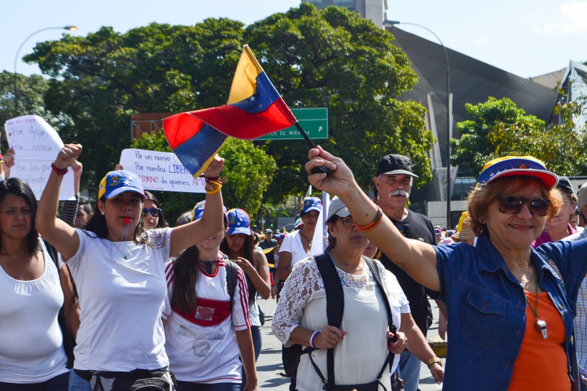 Joukko ihmisiä kulkee kadulla heiluttaen käsiään ja Venezuelan lippuja.