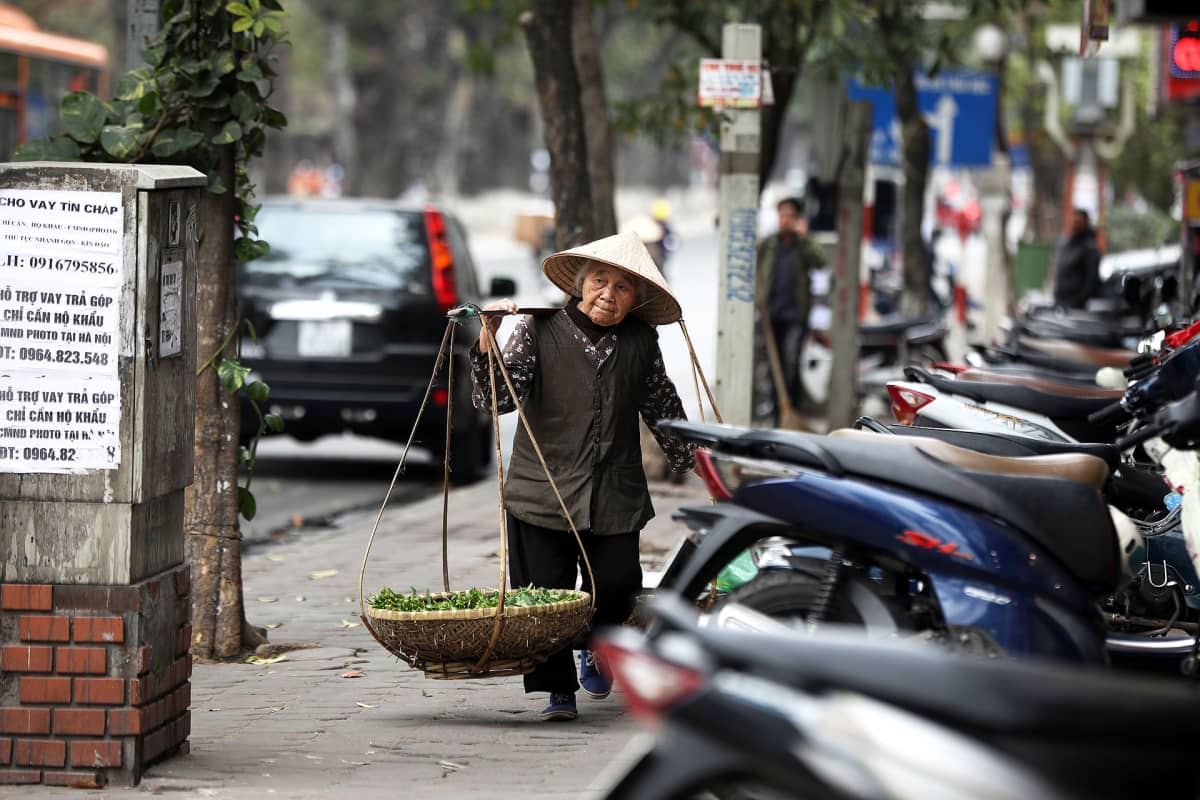 Nainen kantaa vihanneskuormaa kadulla Hanoissa Vietnamissa.