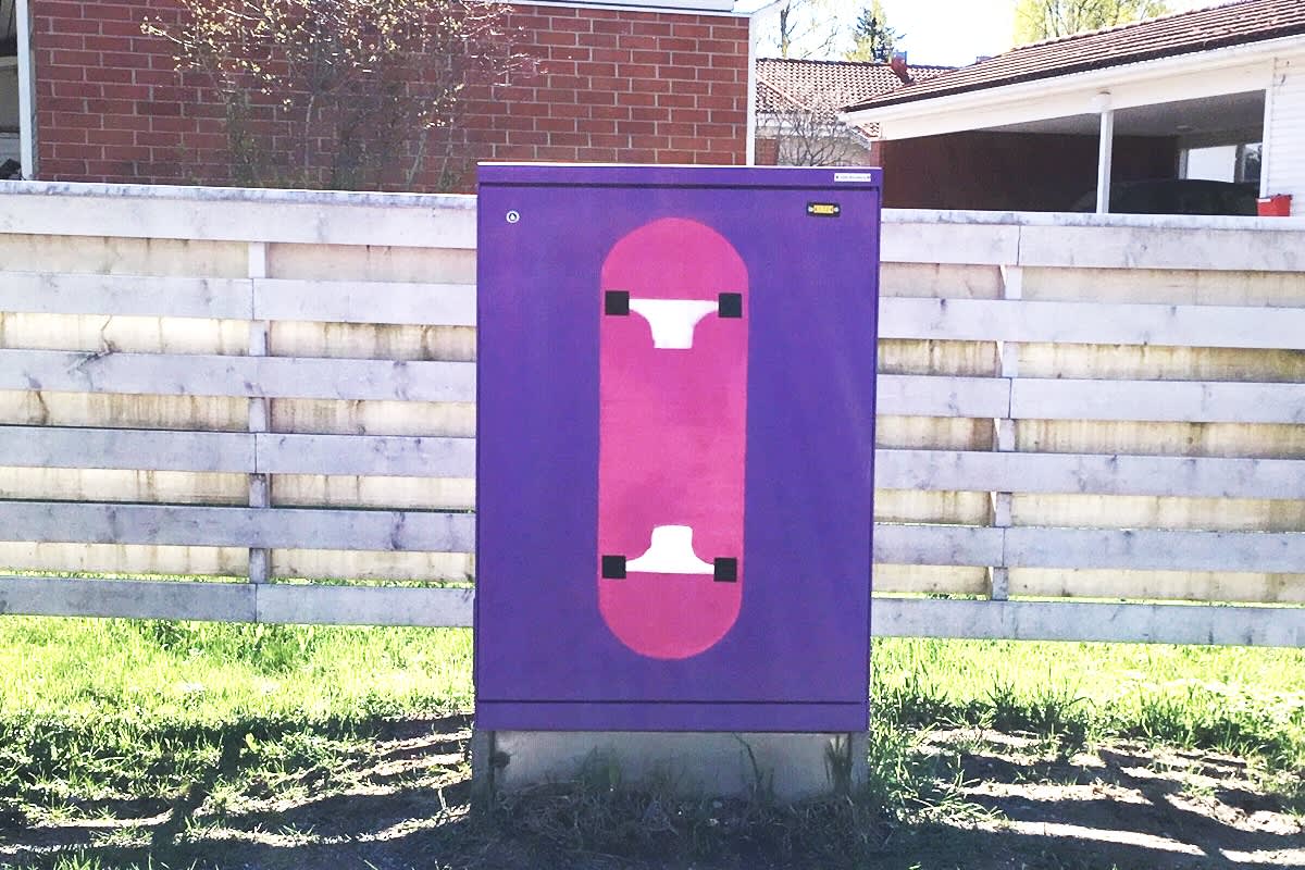 Maalattu sähkökaappi. Kuvassa violetilla pohjalla vaaleanpunainen skeittilauta.