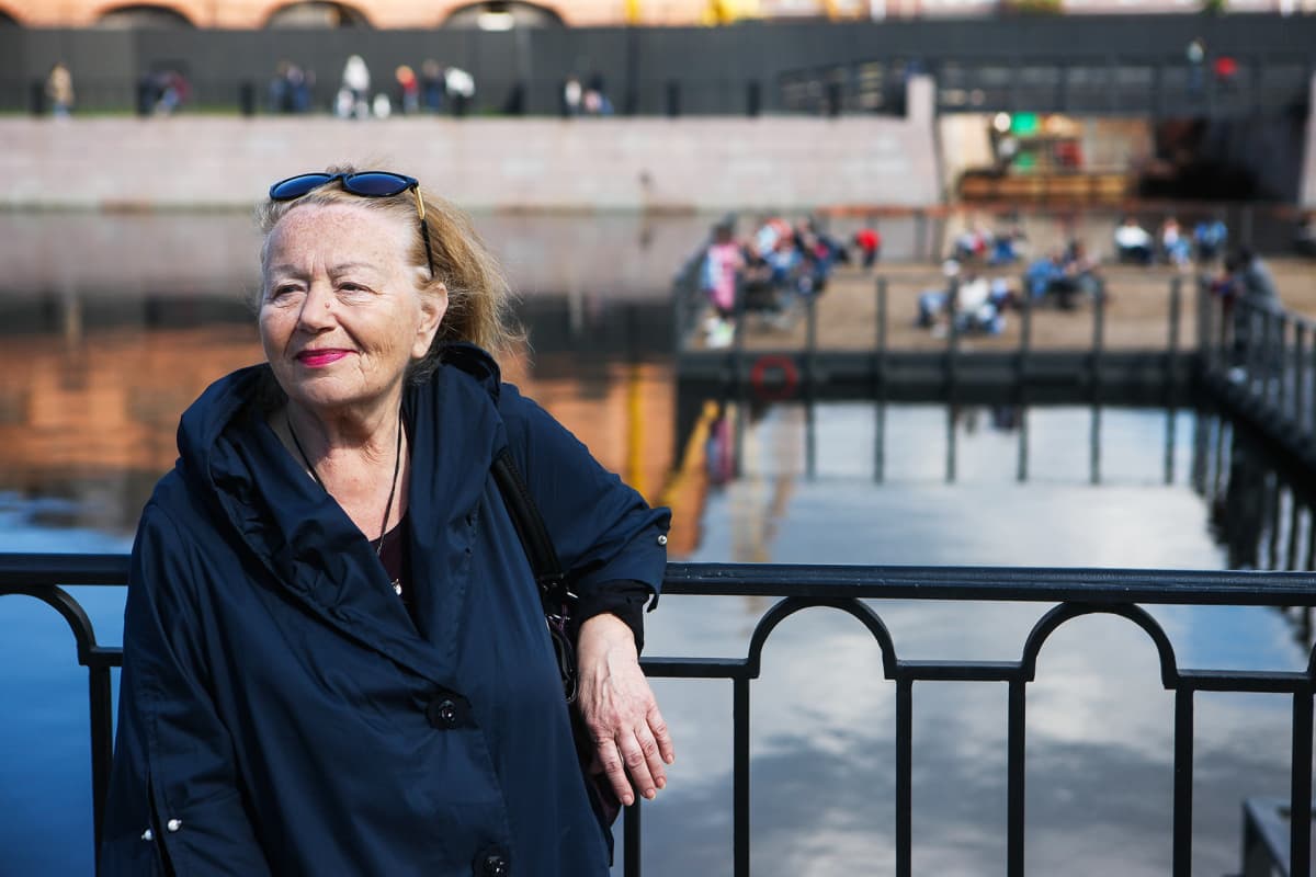 Tamara nojaa aitaan, jonka takana on vesiallas ja hiekkaranta.