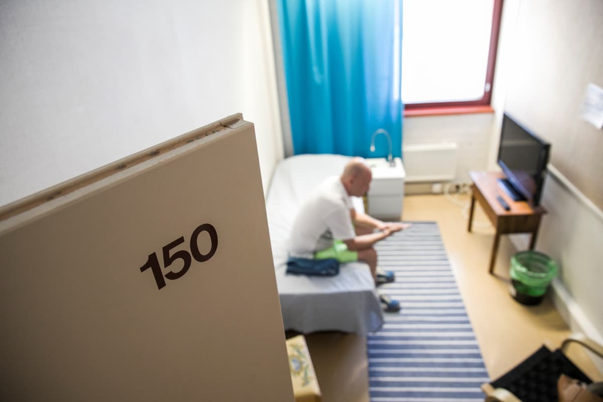 Mies istuu päihdehoitolaitoksen huoneen sängyllä.
