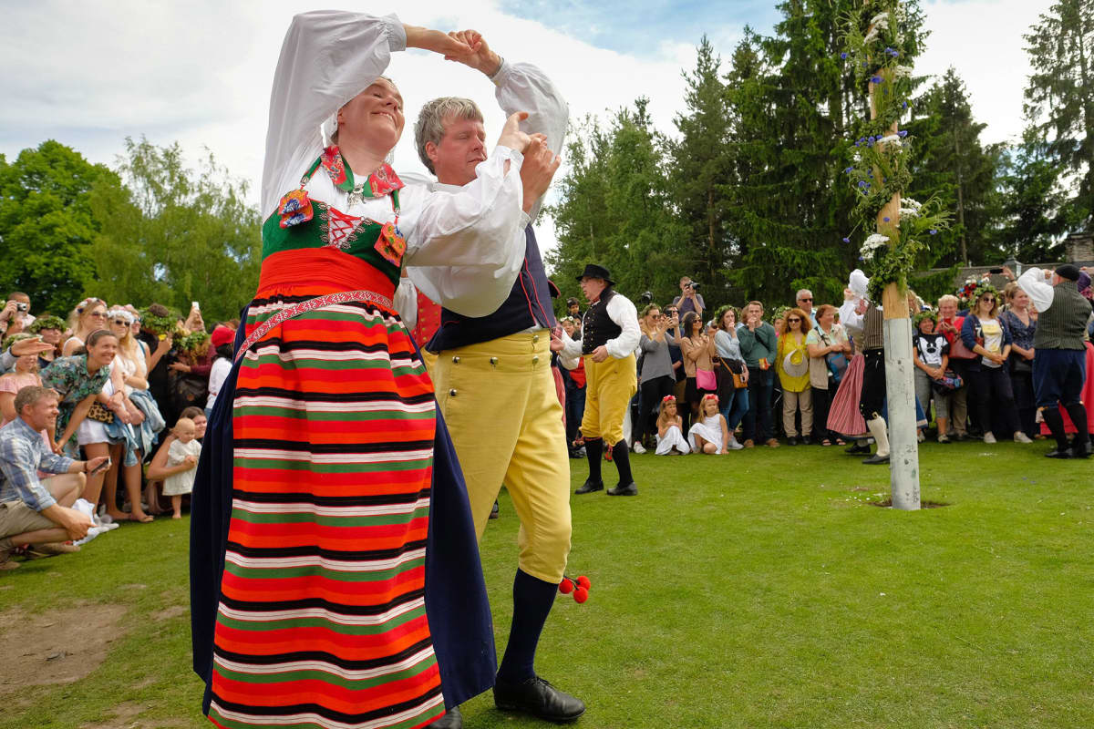 Kansallispukuihin pukeutuneet juhlijat tanssivat juhannussalon ympärillä Tukholmassa.