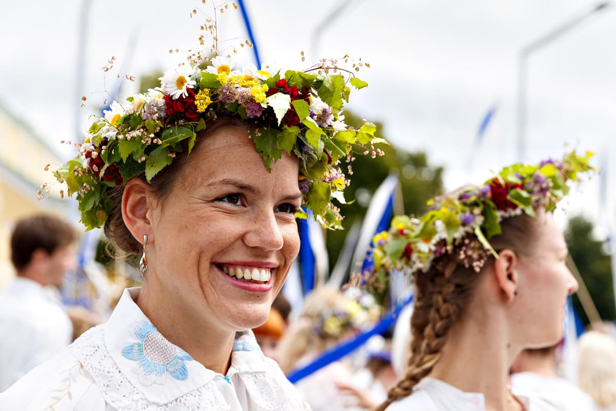 Kaksi naista kulkueessa kukkaseppeleet päässään.