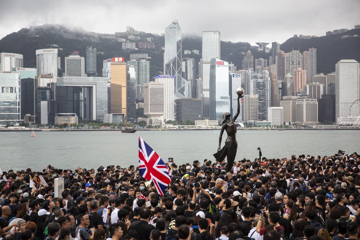 Valtava ihmisjoukko. Keskellä patsas. Taustalla Hongkongin pilvenpiirtäjiä.