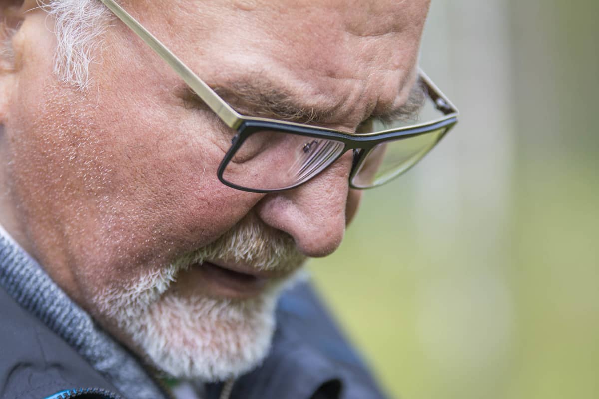 Silmälasipäinen mies katsoo lähikuvassa maahan päin