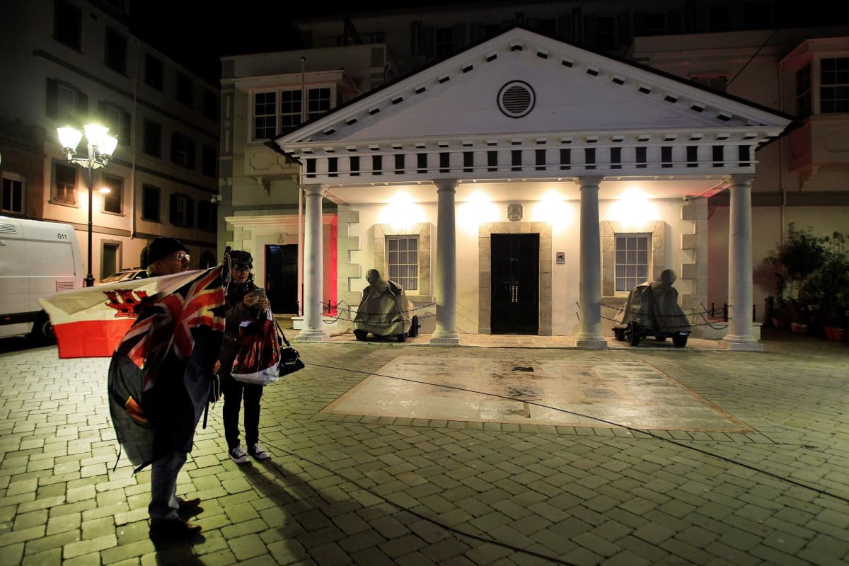 Gibraltarin aluehallinnon rakennus. Edustalla kaksi lippuja heiluttavaa ihmistä.