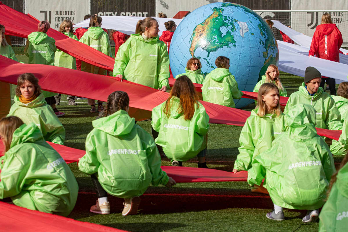 Greenpeacen haalareihin pukeutuneita mielenosoittajia, joilla on punaisia nauhoja ja suuri karttapallo.