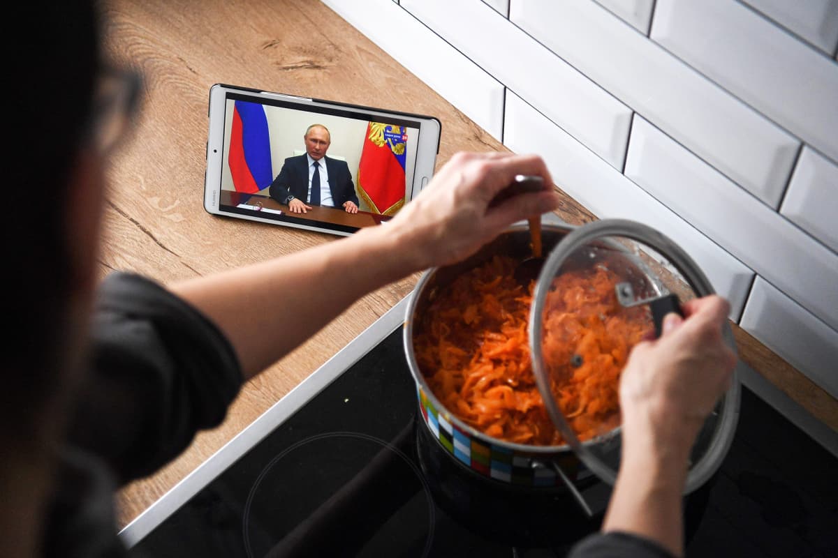 Venäläisnainen laittaa ruokaa ja katsoo samalla kännykästä presidentti Vladimir Putinin puhetta.