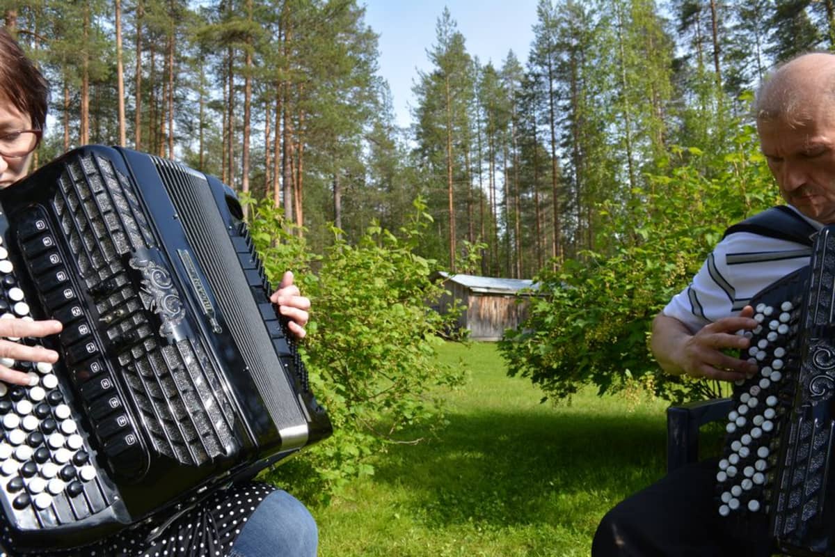 Lea Taipale ja Martti Turunen soittavat haitareita puutarhatuoleissa pihamaansa keskellä.