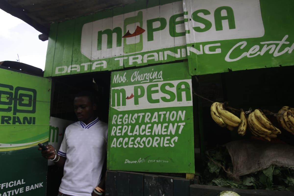 Mies näprää puhelintaan M-Pesa-kioskin edessä Nairobissa.