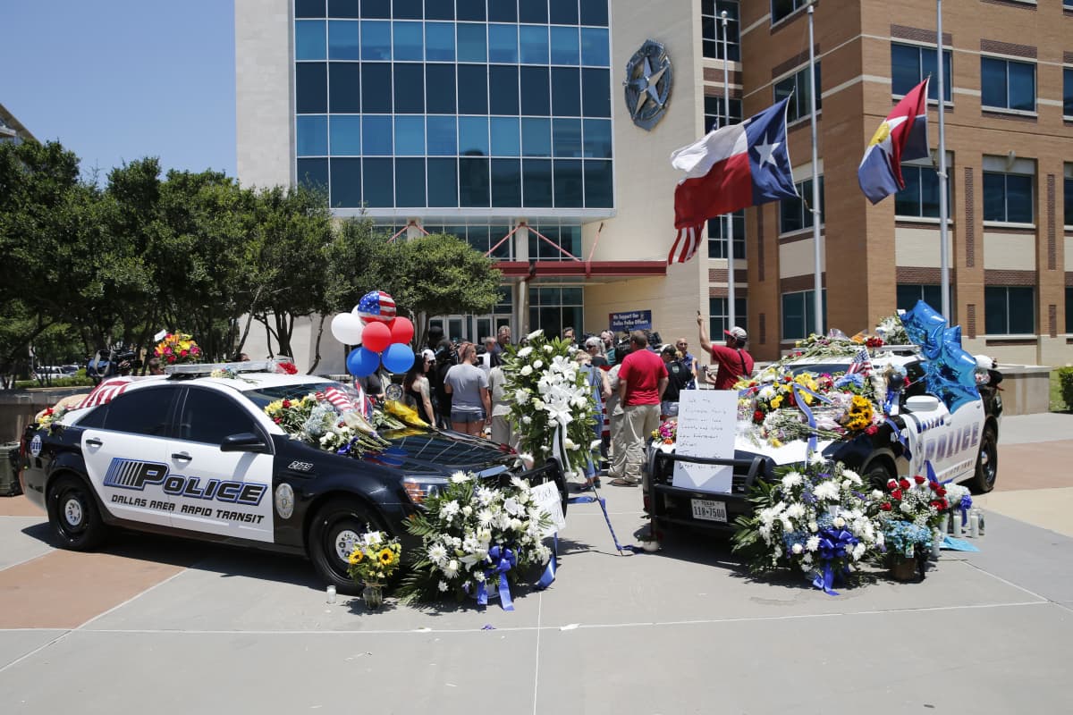 Dallasin poliisilaitoksen edustalla osoitettiin kunnioitusta surmansa saaneille poliiseille. Dallas, Teksas 8.7. 2016. Kuvassa poliisiautoja, joissa kukkia, lippuja, ilmapalloja ja kortteja.