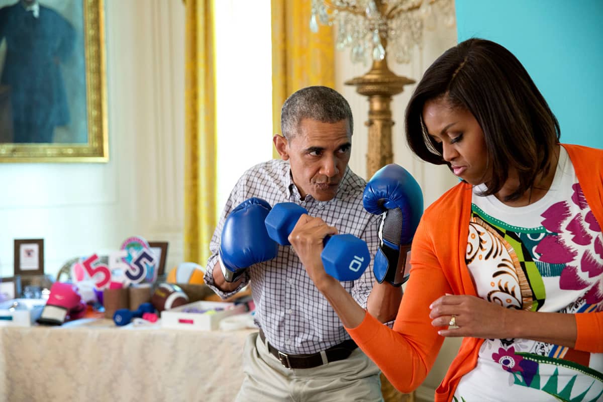 Presidentti Barack Obama hassuttelee nyrkkelyhanskat kädessä vaimonsa Michellen kanssa, joka pitää toisessa kädessään käsipainoa.