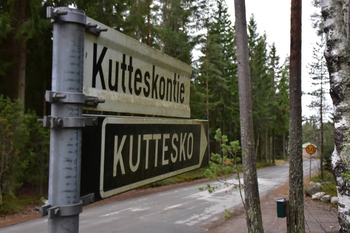 Kaksi tienviittaa. Ylimmässä lukee Kutteskontie ja alimmassa Kuttesko. Taustalla mestää ja kaukana häämöttää talo.