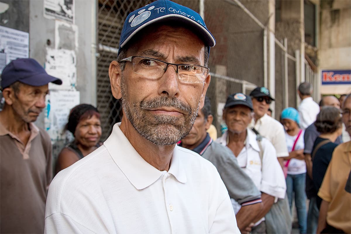 Vanhempi mies lippalakki päässä jonossa Caracasissa, Venezuelassa.