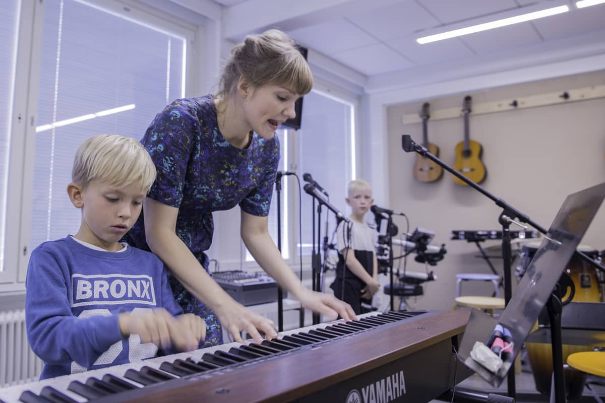 Musiikinopettaja Ella Rosenlund neuvoo Ekko Pakkasta koskettimissa. Taustalla laulaa Niilo Käenmäki.
