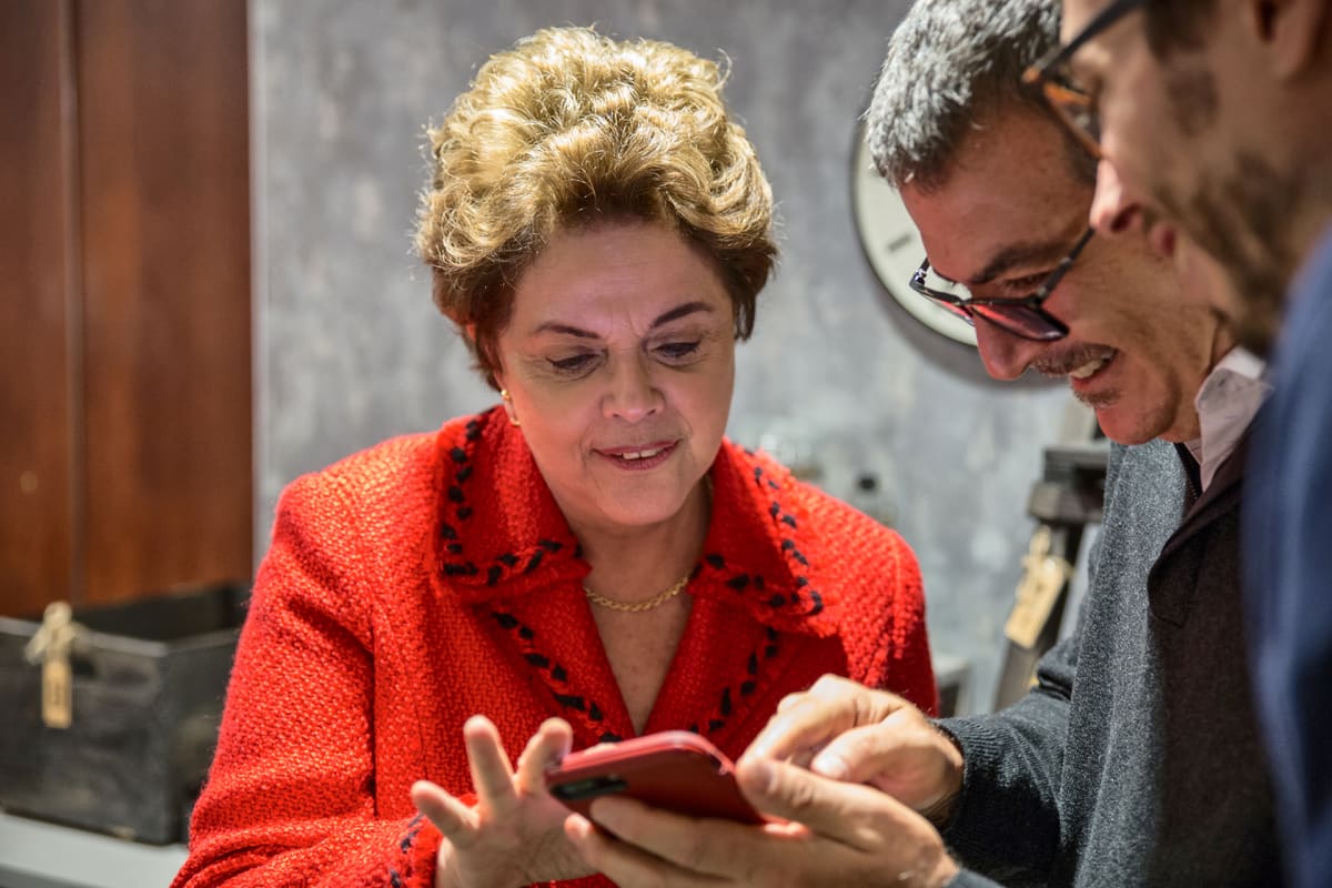 Dilma Rousseff katselee älypuhelinta kahden miehen kanssa.