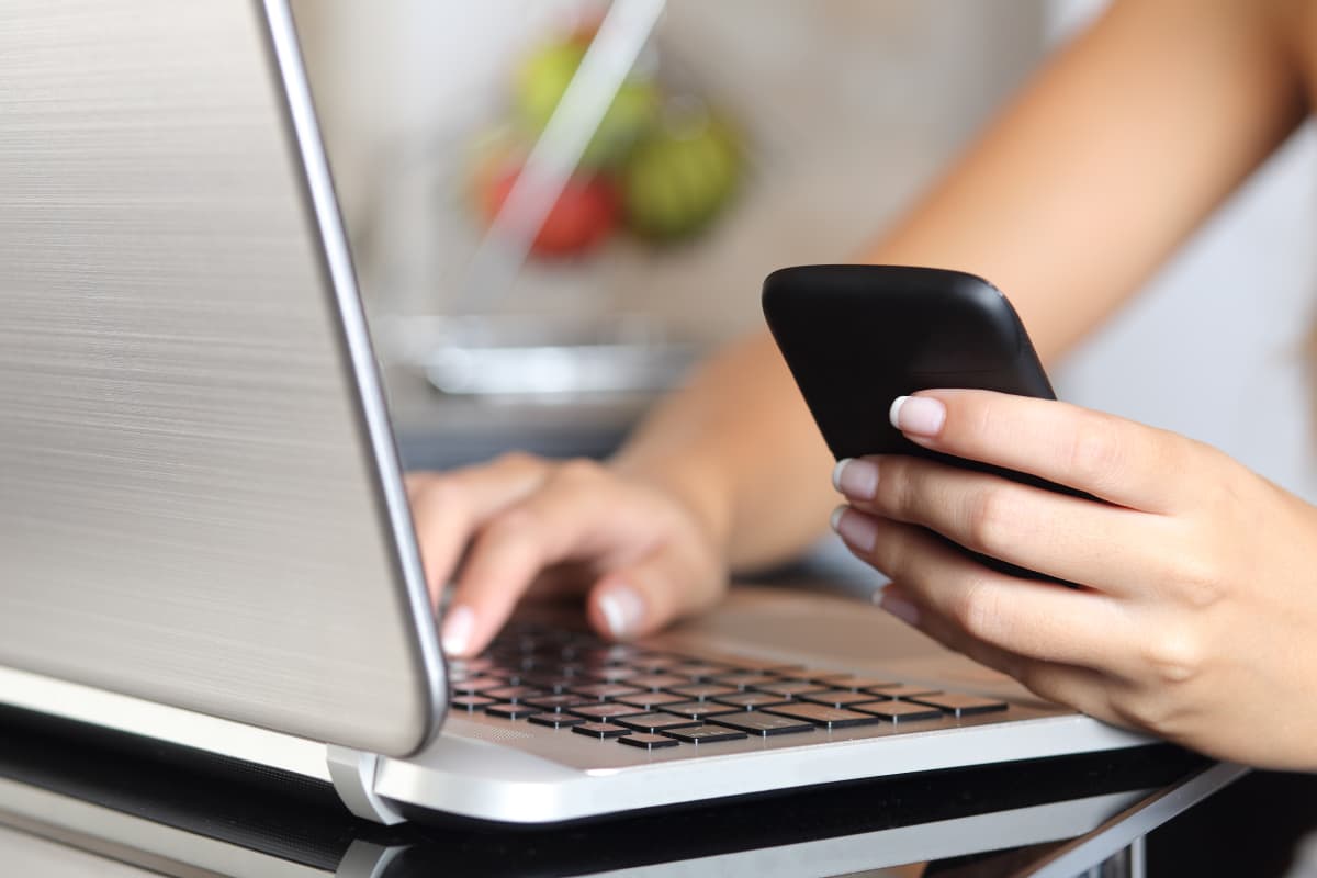 Kvinna håller i mobiltelefon och skriver på laptop