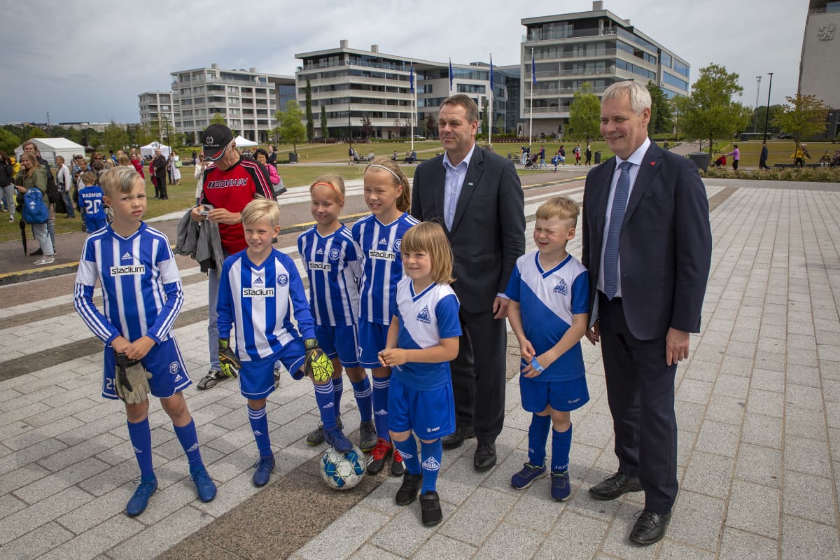 Jan Vapaavuori ja Antti Rinne poseeraavat jalkapallojunioreiden kanssa.