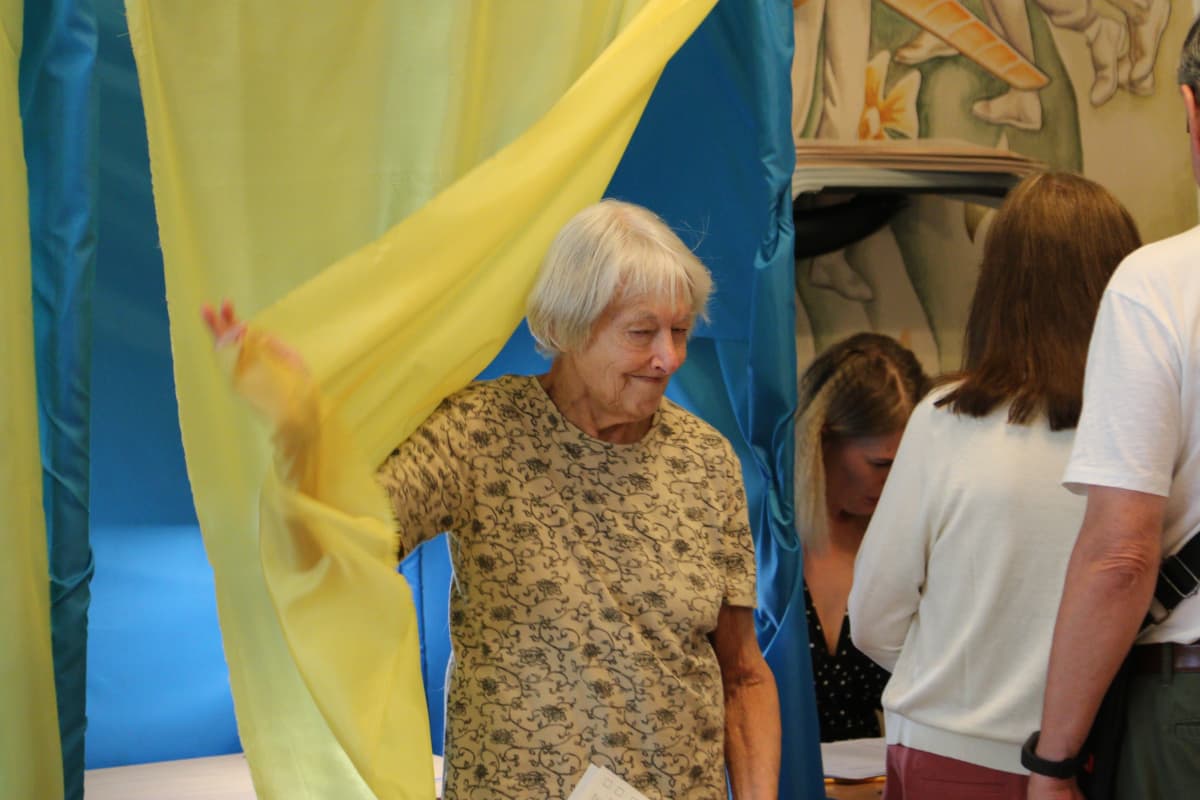Vanhempi rouva tulee ulos äänestyskopista. Koppien verhot ovat Ukrainan lipun väreissä: keltaisia ja sinisiä.